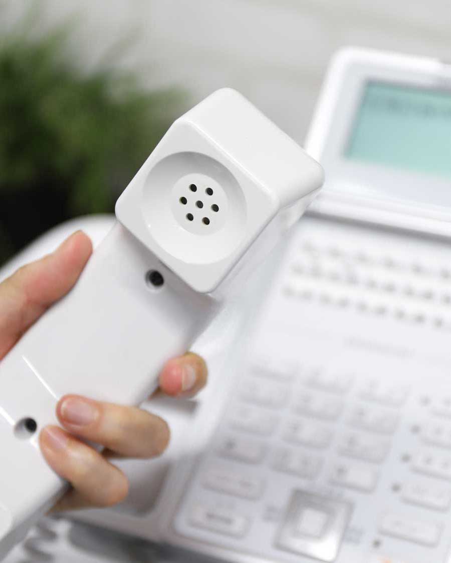 ビジネスフォンの受話器を取って電話対応をする手元